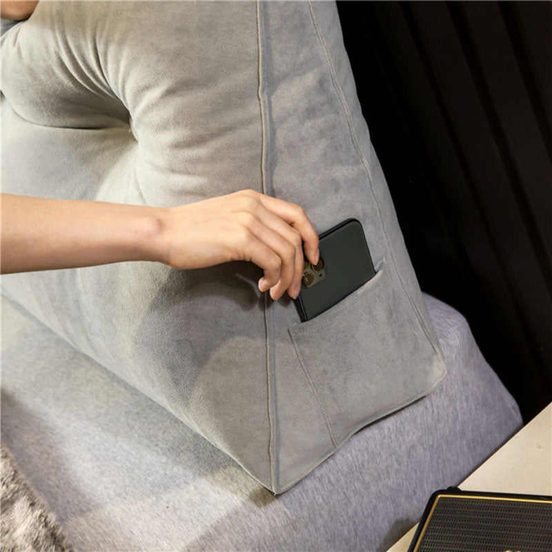 detail of a grey velvet wedge pillow with a phone in the side pocket.