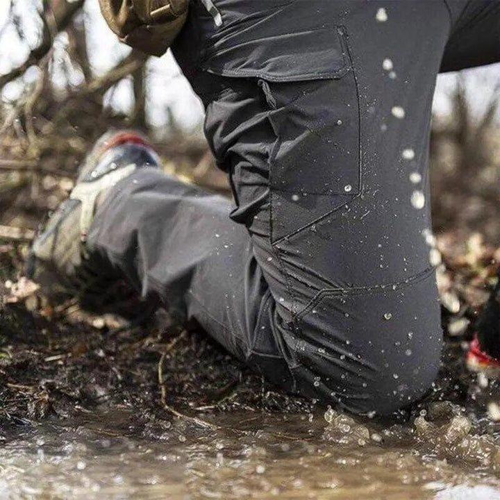 Men's gray cargo pants close-up with water beading on the fabric in a muddy stream.