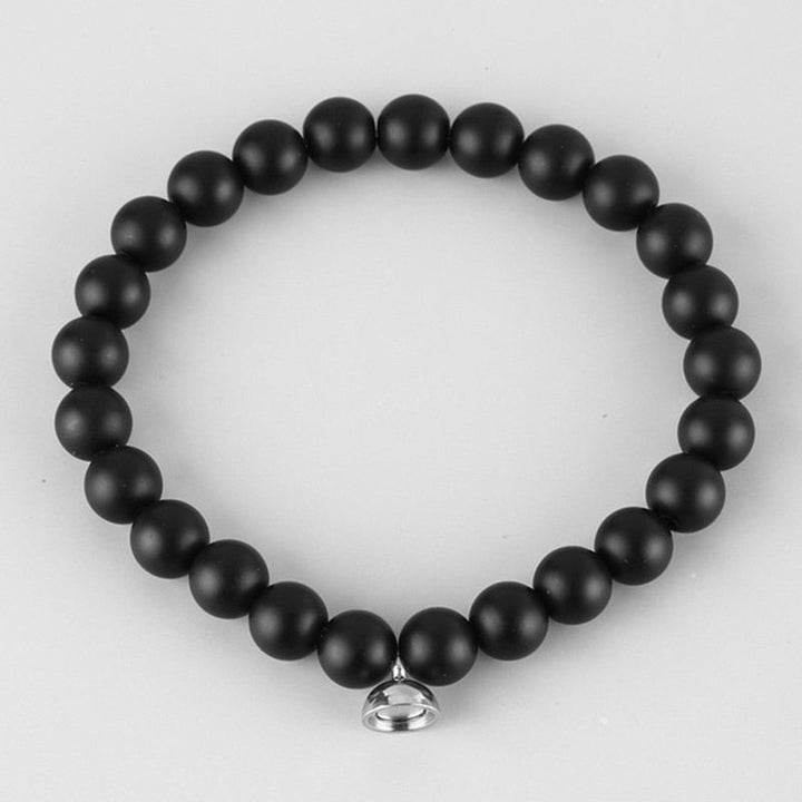 Matte black bead bracelet with a small silver magnetic clasp, laid flat on a light gray background 2