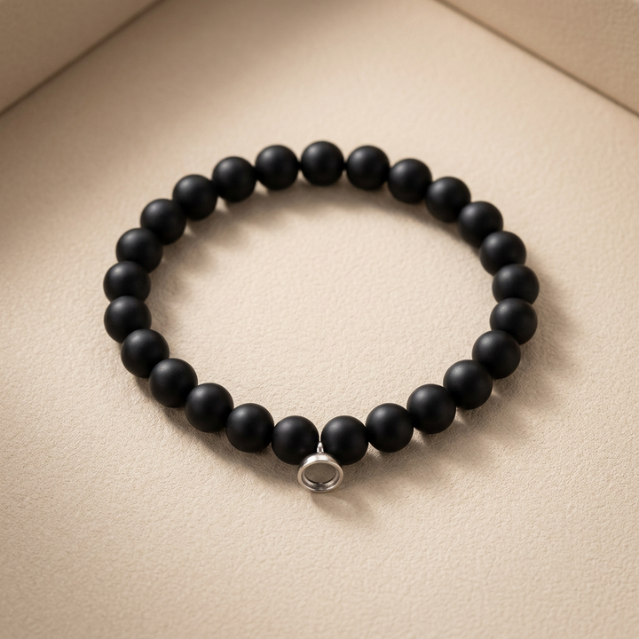 Stretch bracelet of matte black round beads with a small silver ring charm, lying on a beige surface 1