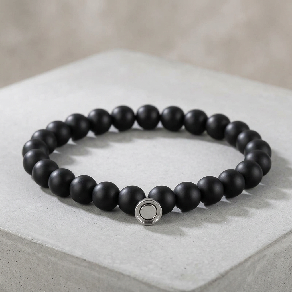Matte black bead bracelet with a round silver clasp, displayed on a light gray concrete block 2