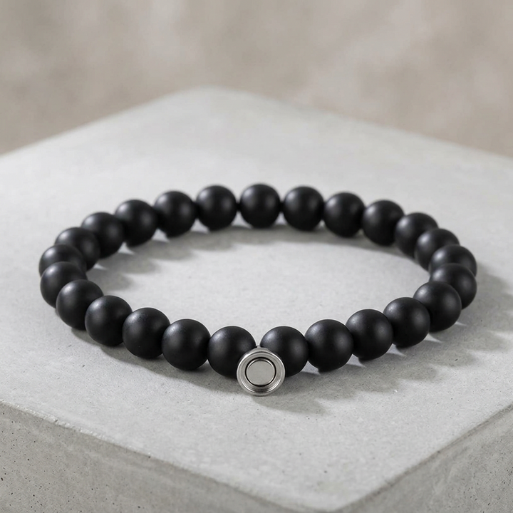 Matte black bead bracelet with a round silver clasp, displayed on a light gray concrete block 2