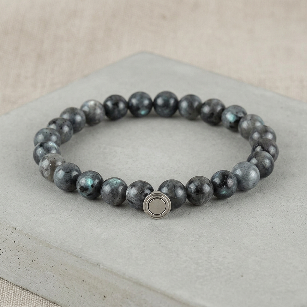 Dark gray beaded bracelet with teal flashes in the stones and a silver clasp, on a concrete slab 4