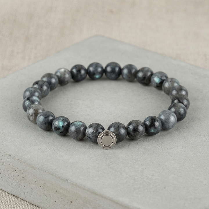 Dark gray beaded bracelet with teal flashes in the stones and a silver clasp, on a concrete slab 4