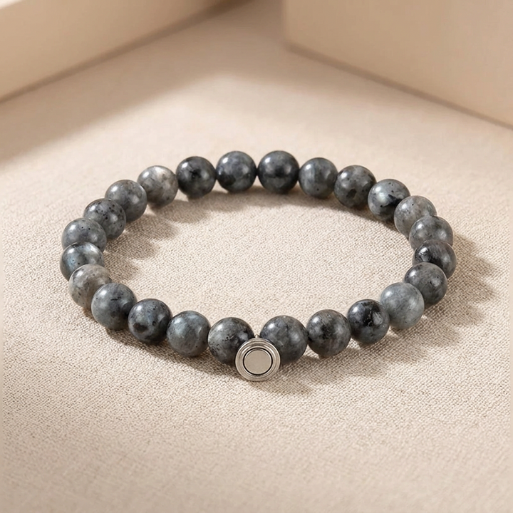 Bracelet of dark gray speckled stone beads with a round silver magnetic clasp bead, resting on a beige surface 3