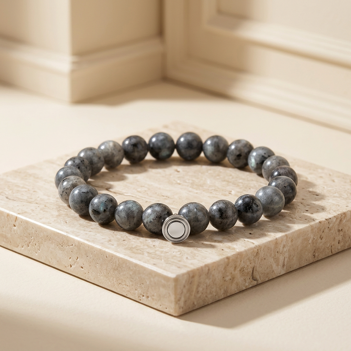 Gray speckled stone bead bracelet with a round silver clasp, resting on a cream travertine slab 1