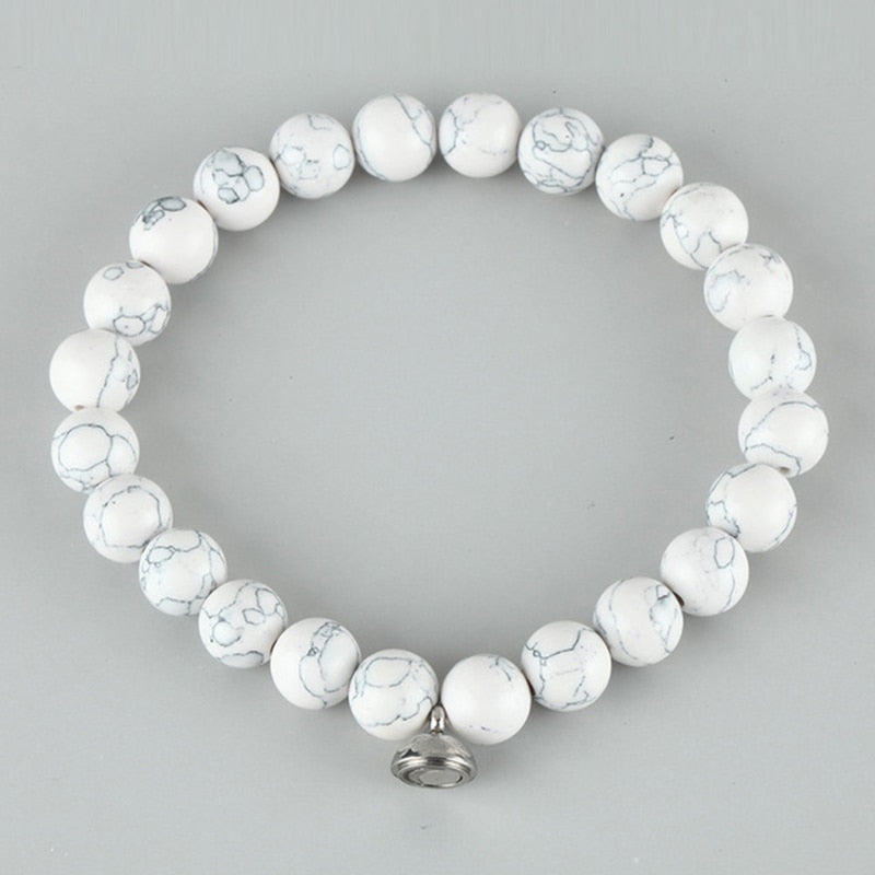 White beaded stretch bracelet with gray marbled veining and a small silver magnetic charm, photographed on a gray background 3