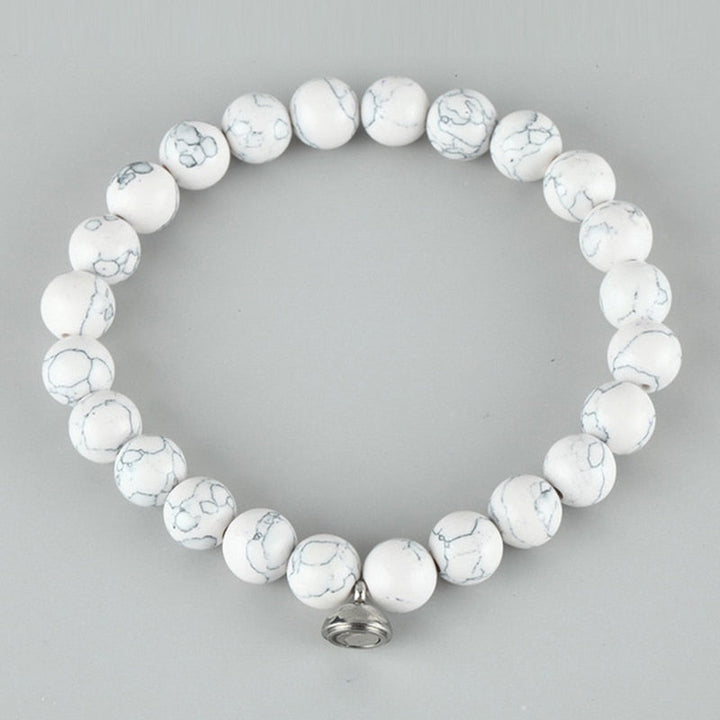 White beaded stretch bracelet with gray marbled veining and a small silver magnetic charm, photographed on a gray background 3
