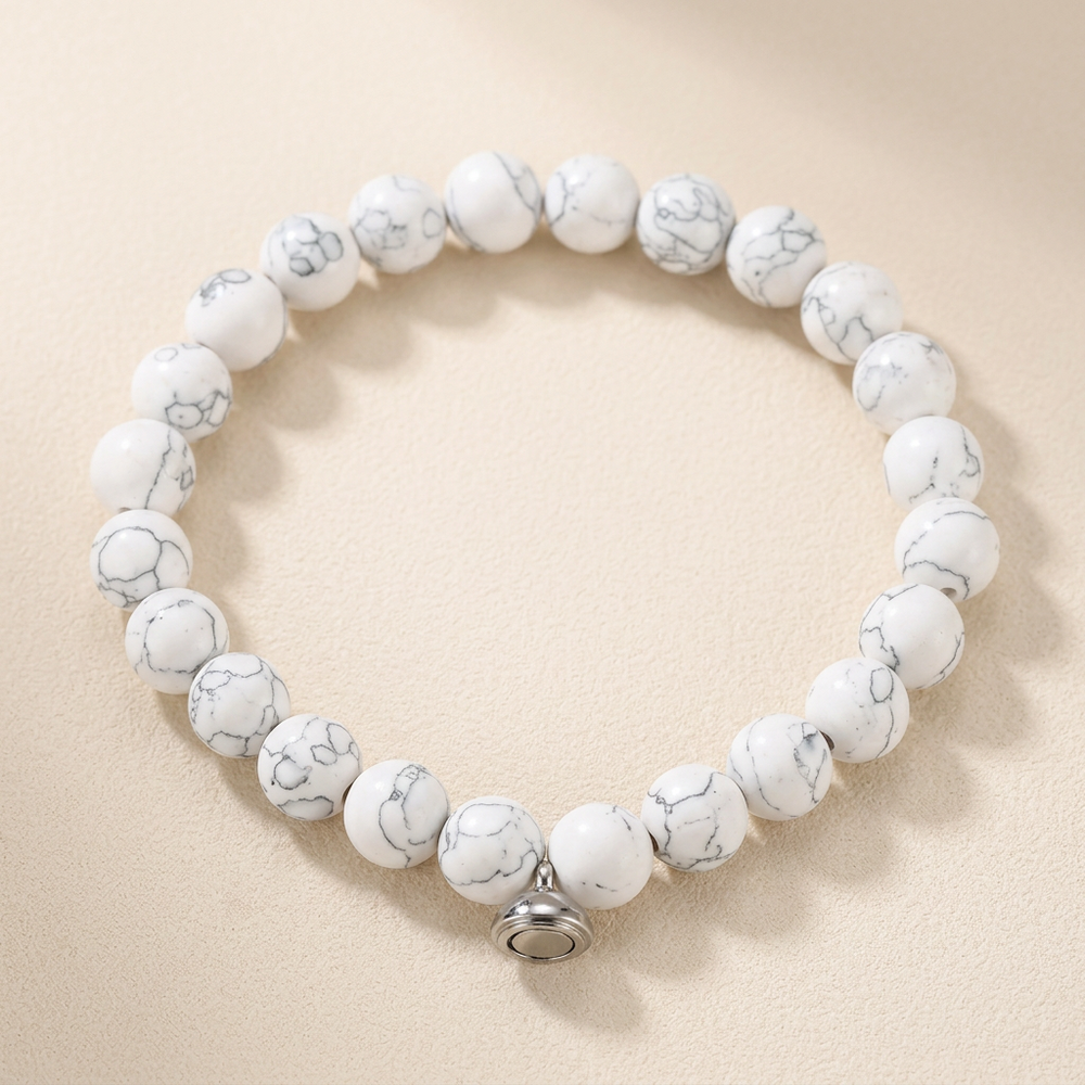 Bracelet of white beads with gray marbled veining and a silver magnetic clasp, laid flat on a cream background 2