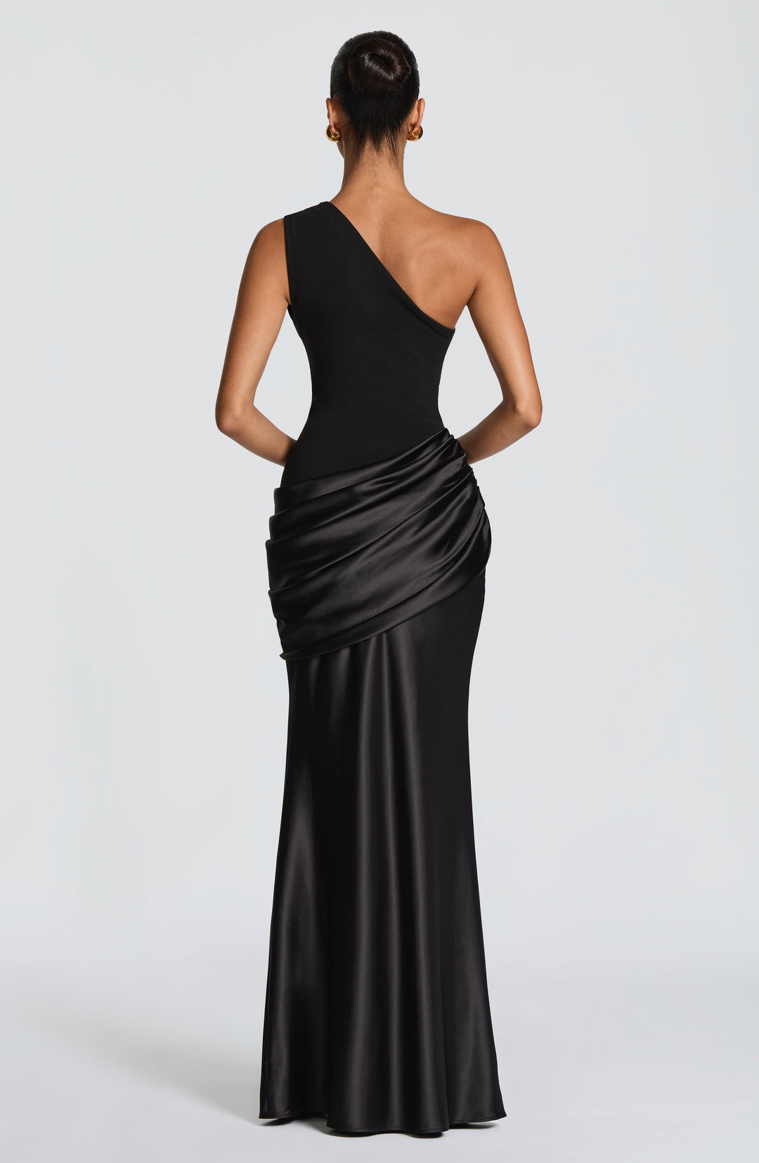 Front view of the black one-shoulder satin maxi dress with a pleated bodice, draped hip panel and gold ball earrings. 40