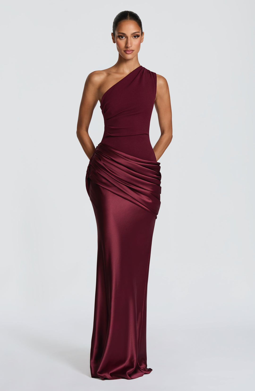 Burgundy one-shoulder dress against a white wall, one arm behind her head and the other hand in a pocket. 38
