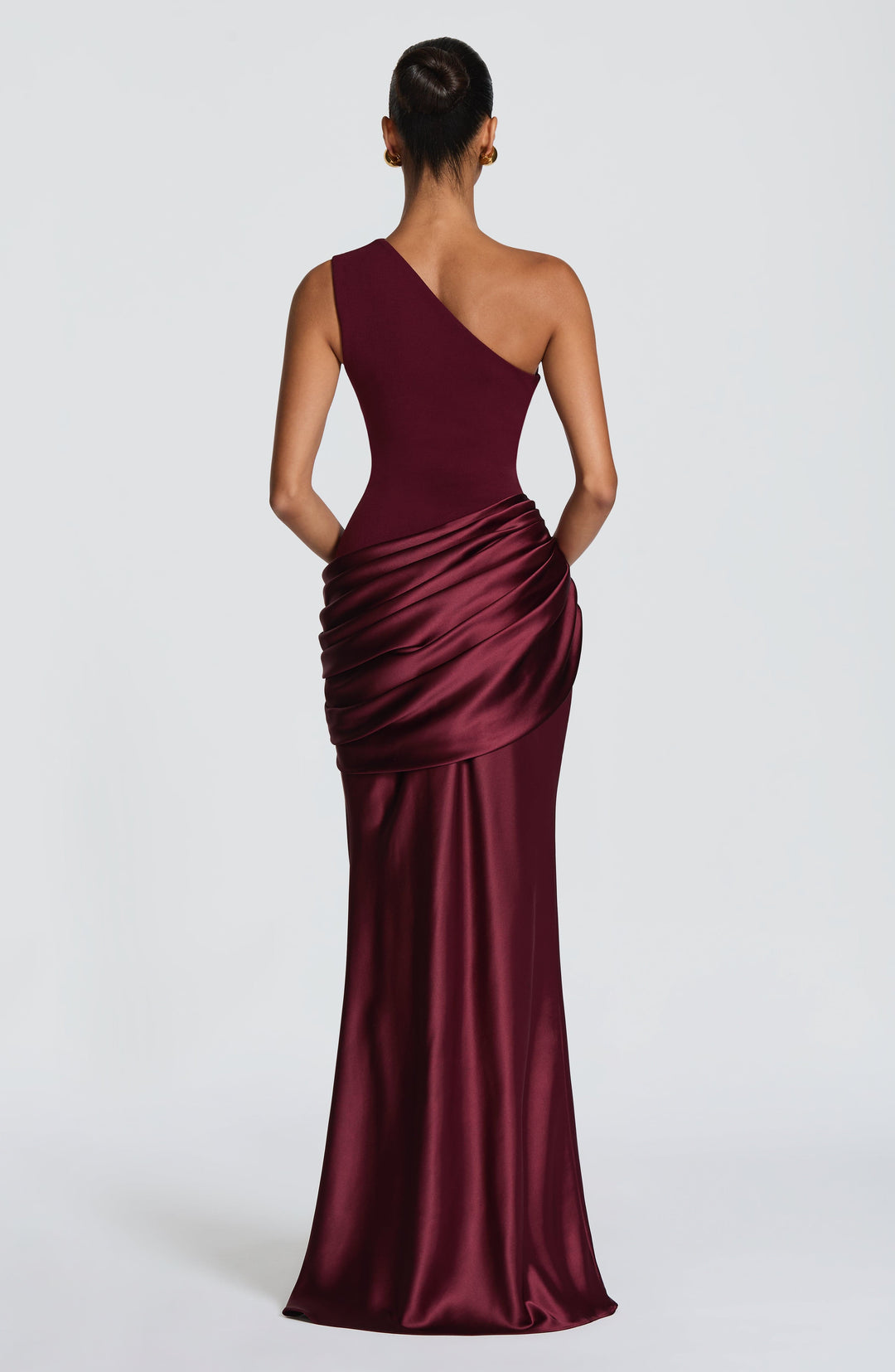 Burgundy one-shoulder maxi dress, model leaning against a wall with one arm raised behind her head, showing the shiny satin skirt. 32