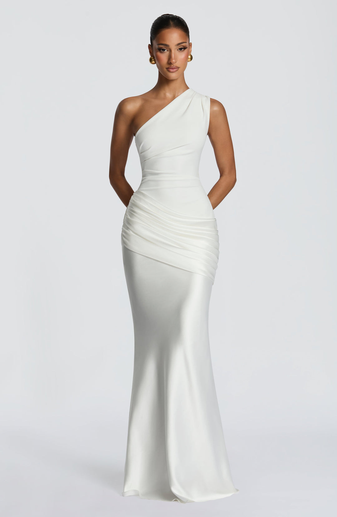 Ivory one-shoulder maxi dress from the front, hands behind the back, showing the ruched satin drape and fitted waist. 25