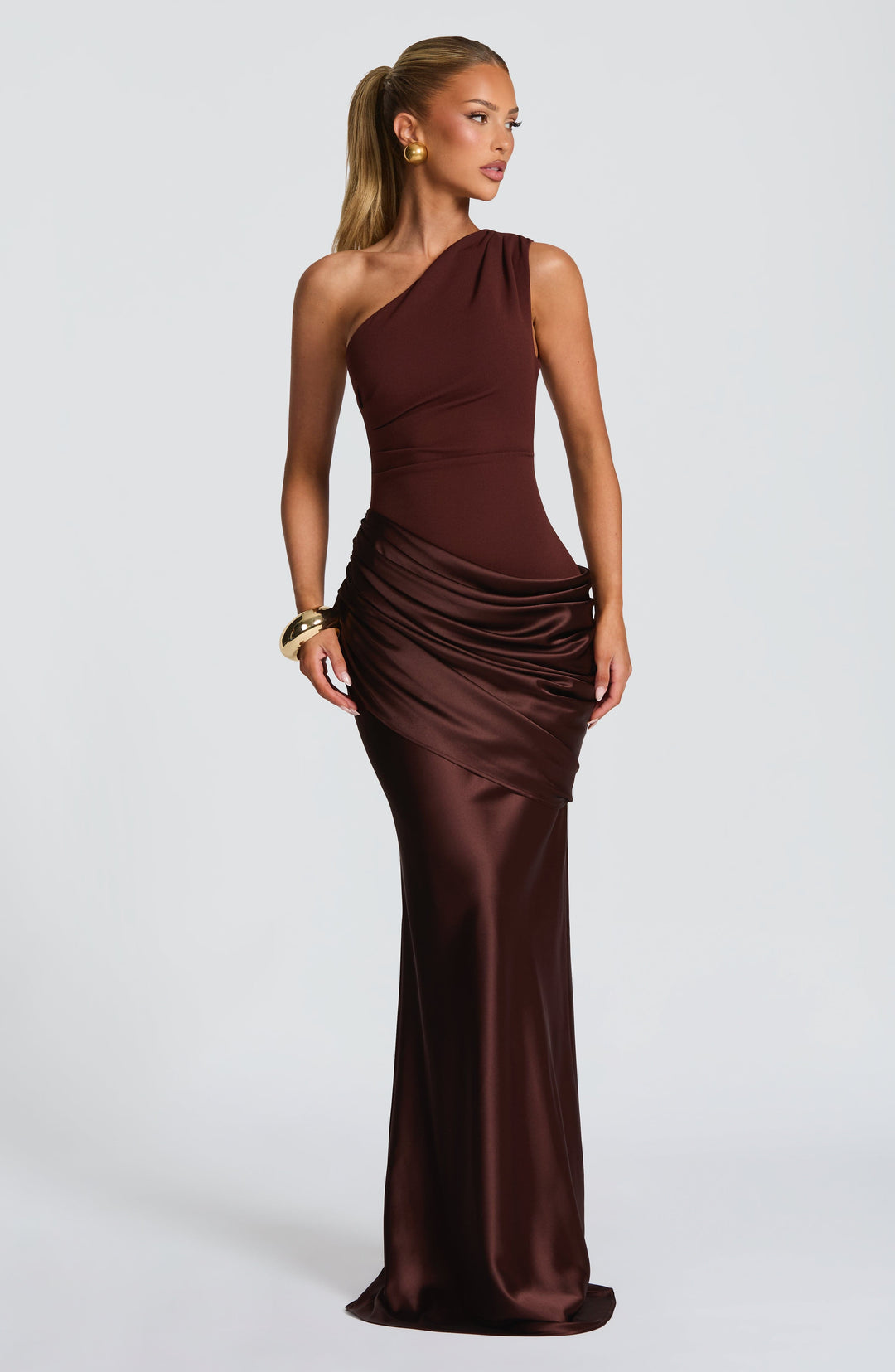 Dress in deep chocolate brown on a blonde model with a high ponytail, gold earrings and a gold cuff, three-quarter view. 25