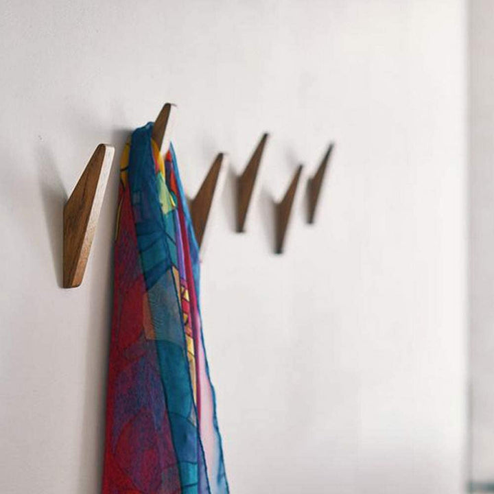Angled darker wooden hooks lined up on a white wall, with a colorful patterned scarf hanging from one hook. 3