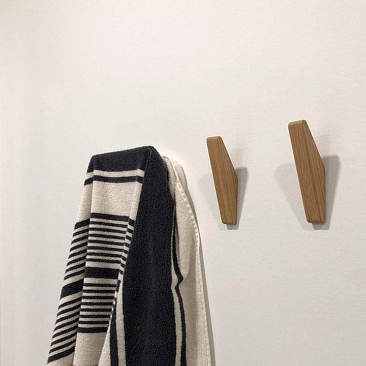Two light wooden hooks on a white wall beside a black and white striped towel hanging from a third hook. 4