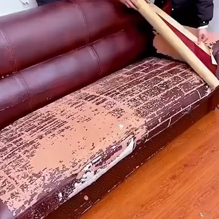 Person laying a roll of leather material over a worn burgundy sofa seat with badly peeling, cracked surface. 22