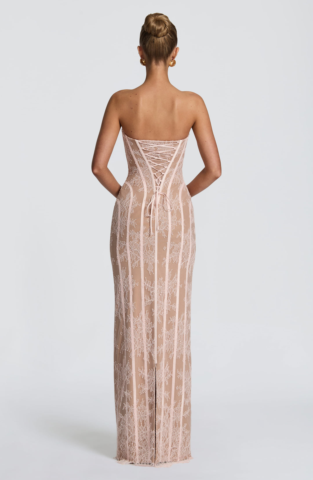 Back view of the blush pink lace dress showing the corset lacing, ribbon ties and a slit at the hem.