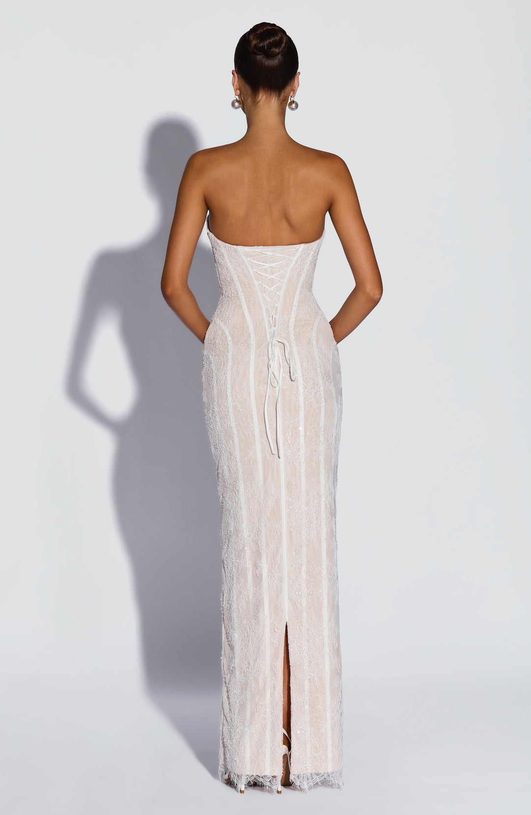 Back view of the white beaded lace dress showing the lace-up corset back, long ties and a center back slit.