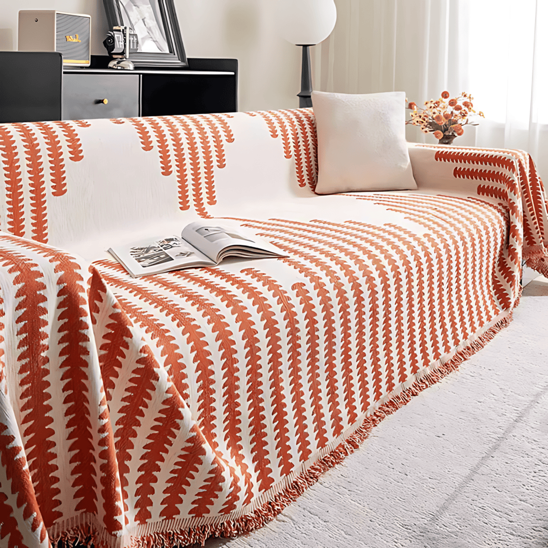 Rust orange and cream graphic-print knit sofa cover another view, with an open magazine and a fringed edge.
