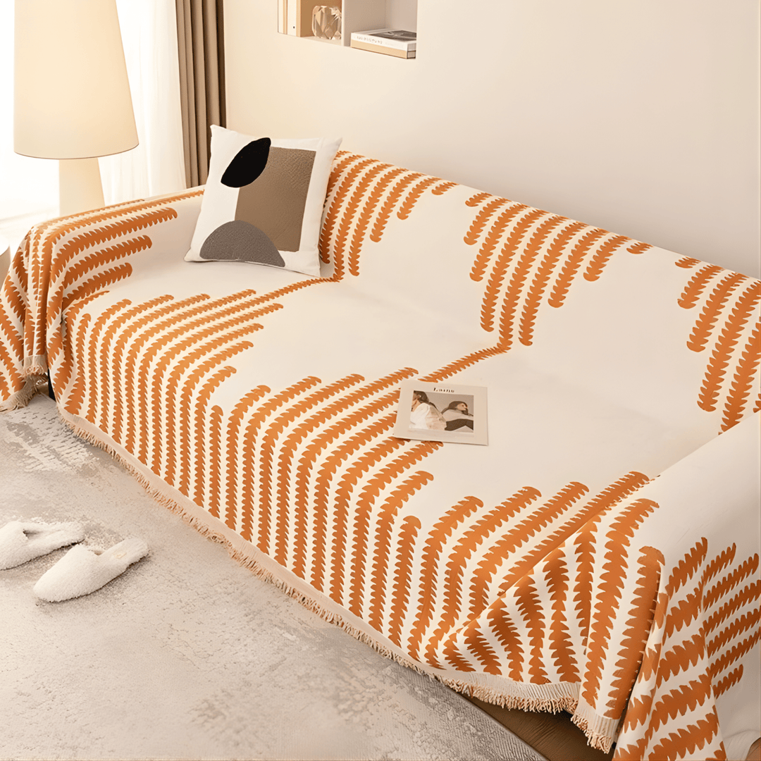 Orange and cream graphic-print knit sofa cover on a sofa, with a cushion and fringed hem.
