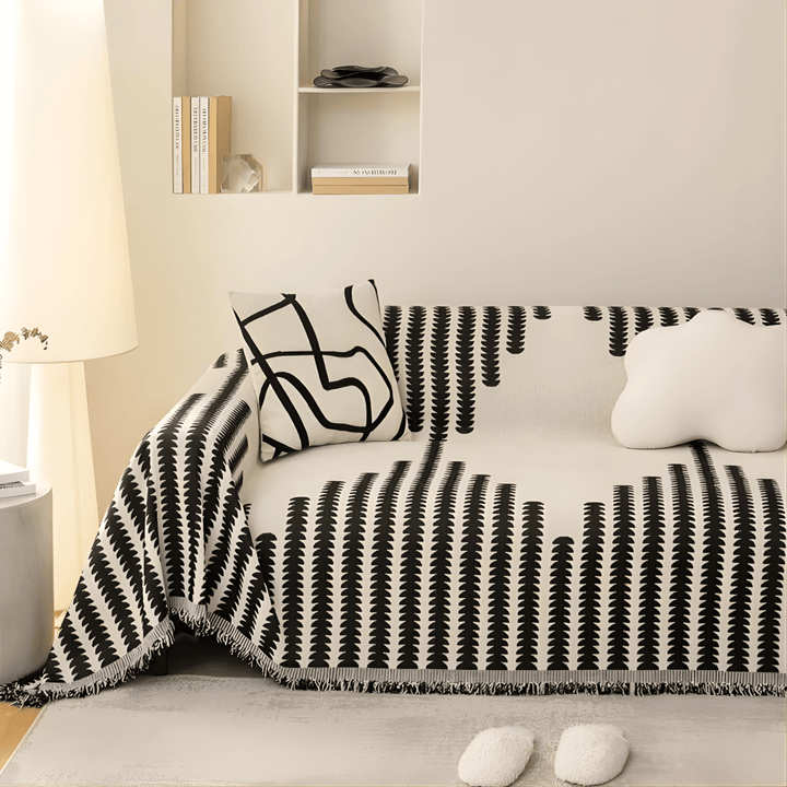 Black and white graphic-print knit sofa cover on a cream sofa, with fringed edges and cushions.