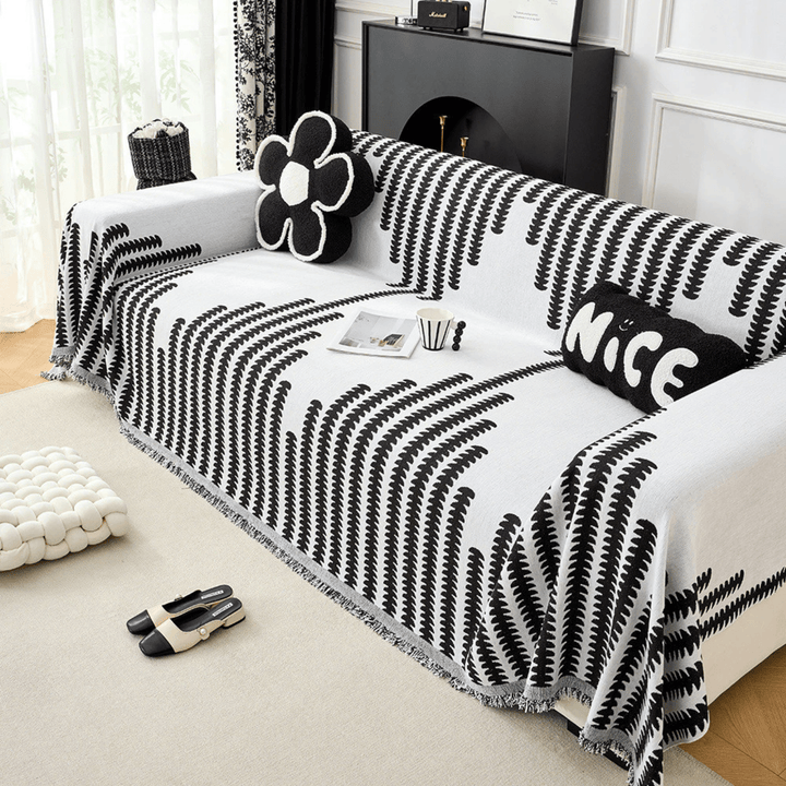 Black and white graphic-print knit sofa cover another view, with cushions and fringe along the edge.