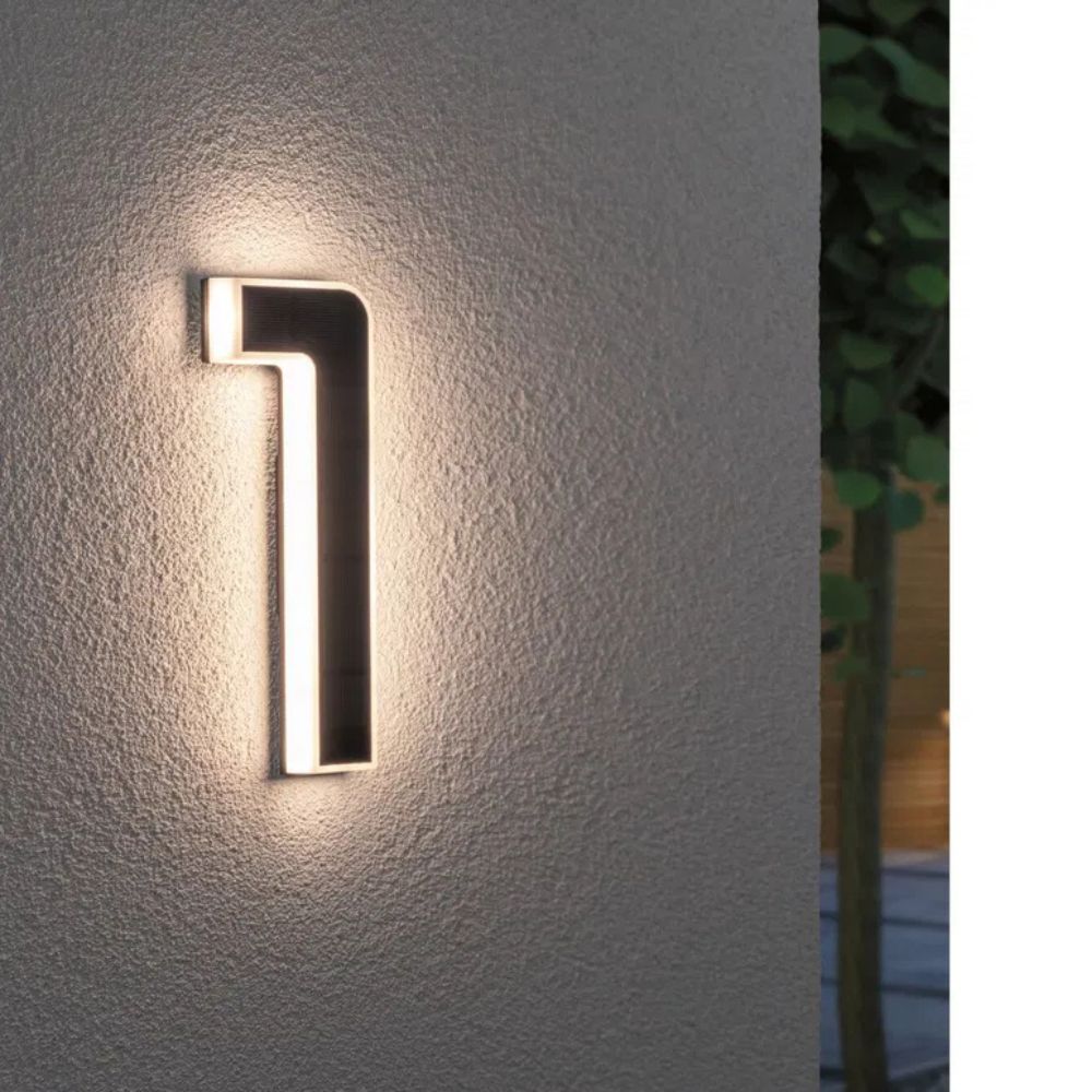 Solar illuminated house number 1 with warm LED edge light and a dark solar panel surface on a gray wall.