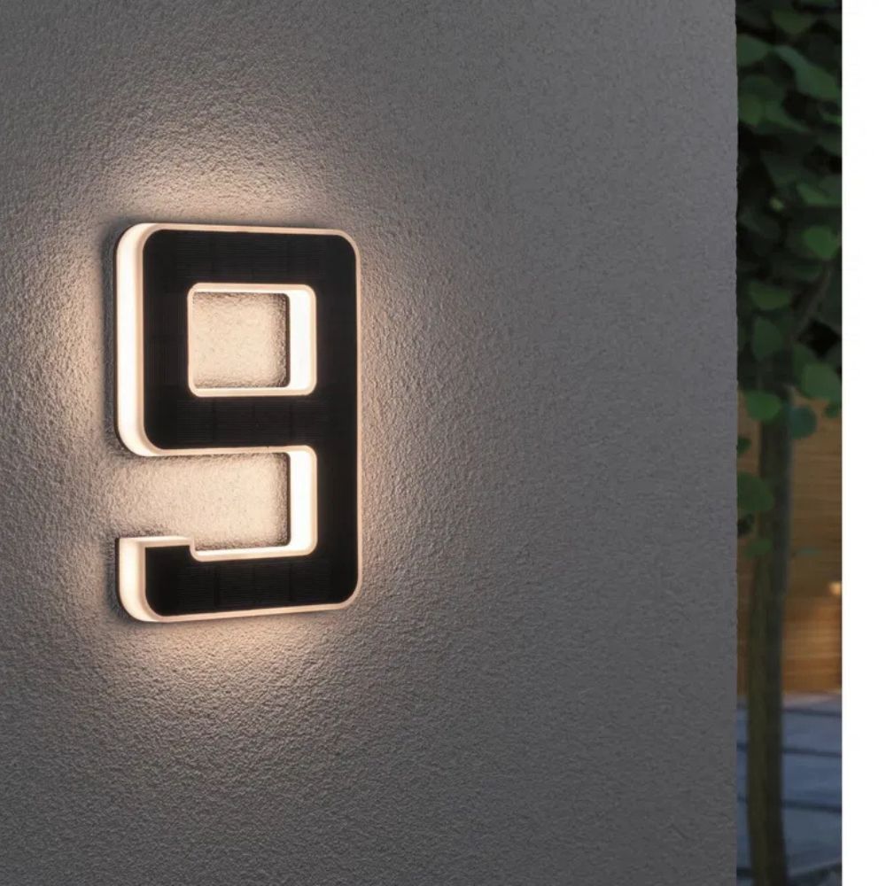 Solar illuminated house number 9 with warm LED outline and a dark solar panel face on a textured gray wall.