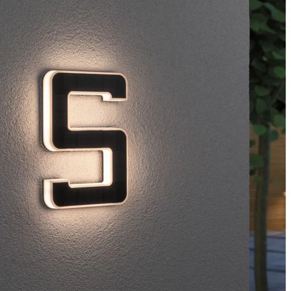 Solar illuminated house number 5 with warm LED glow and a dark solar panel face on a textured gray wall.