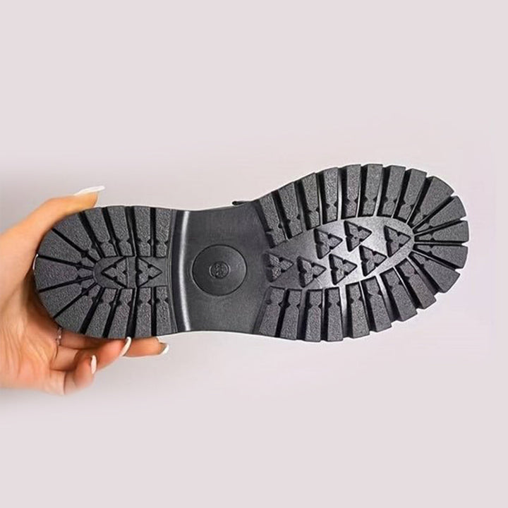 Loafer held upside down showing the black outsole with deep lugs and triangular tread pattern.