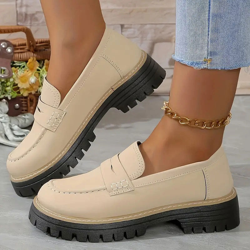 Cream beige loafers with penny straps and thick black platform soles worn with a gold chain anklet.