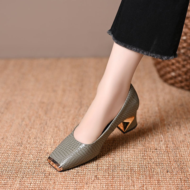 Single gray-green snake-pattern pump on a model's foot, showing the glossy finish, gold toe cap and gold-accented block heel from the side. 3