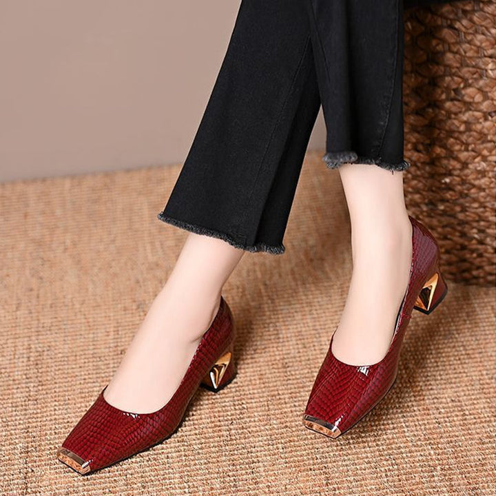 Burgundy red snake-embossed pumps with gold metal toe caps and angular gold-accented heels, worn with black frayed-hem pants on a woven mat. 2