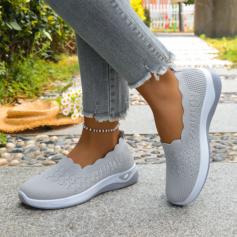 Light gray perforated knit slip-on shoes with a wavy collar and white sole.
