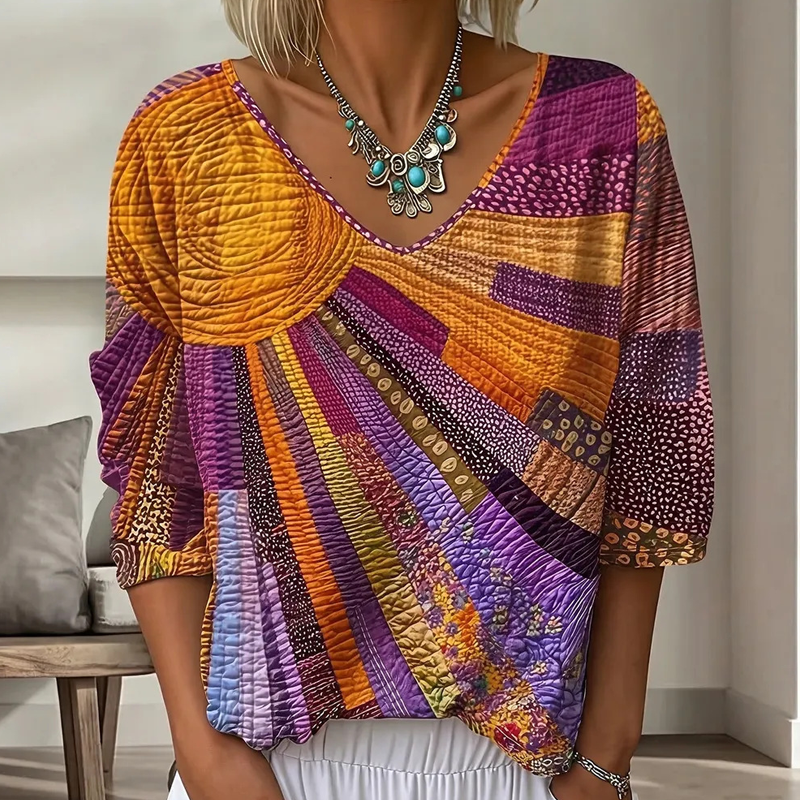 Close-up of the V-neck patchwork blouse in a warm orange, purple and magenta sunburst design, worn with a turquoise statement necklace. 2
