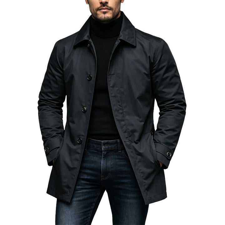 Man wearing the black button-front trench coat over a black turtleneck and dark jeans, hands in pockets. 1
