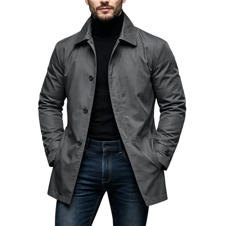 Man wearing the charcoal gray version of the single-breasted coat with a black turtleneck and jeans, hands in pockets. 2