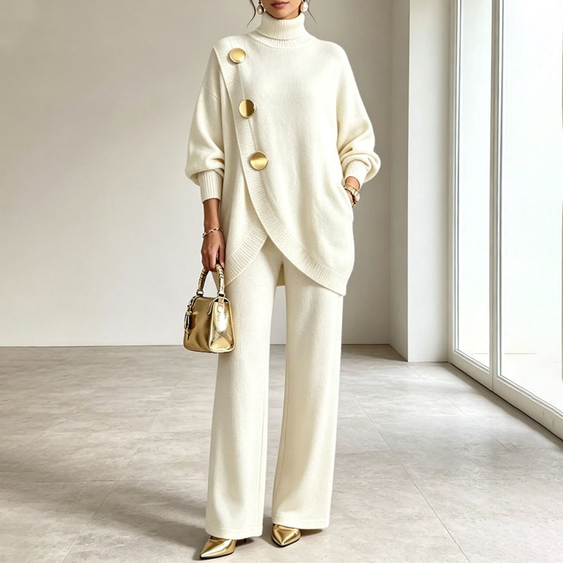 Model wearing the cream knit set with gold buttons and gold pointed heels, one hand in a pocket, holding a gold handbag. 2