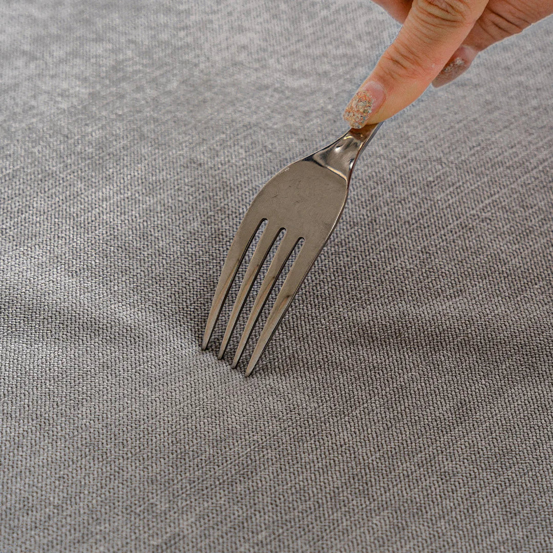 Hand pressing a metal fork into the gray woven fabric surface to show its dense texture. 6