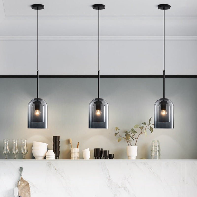 Row of three smoke gray pendants lit above a white marble counter with dishes and a plant 5