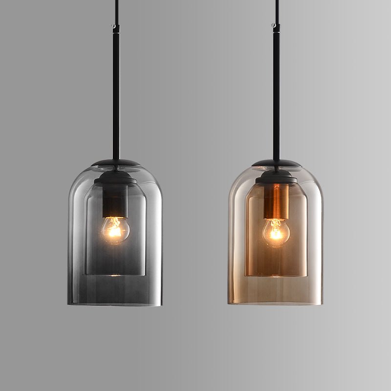 Smoke gray and amber double-glass pendants side by side against a gray backdrop, bulbs lit 2