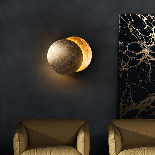 Lamp with gold front disc on a dark wall next to marbled artwork and armchairs 6