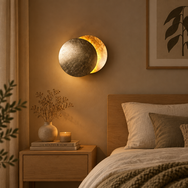 Textured metallic wall lamp glowing above a wooden nightstand with a vase, candle and books in a cozy bedroom 1