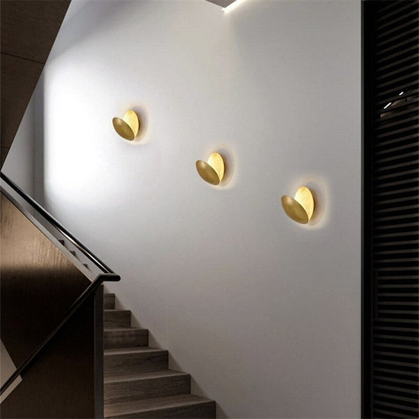 Three gold disc lamps angled on a white stairwell wall, each with a soft halo 7