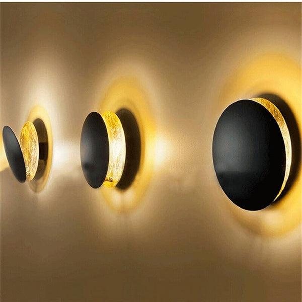 Three black disc lamps in a row on a wall, each casting golden light 10