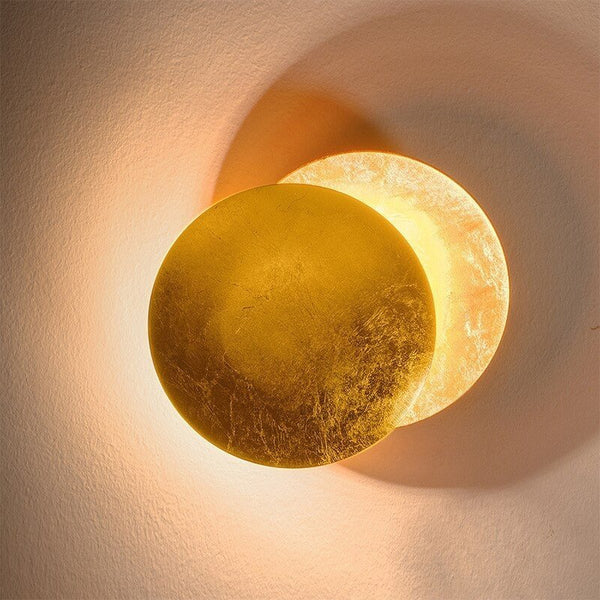Gold front disc and softly lit back disc of the wall lamp on a textured light wall 12