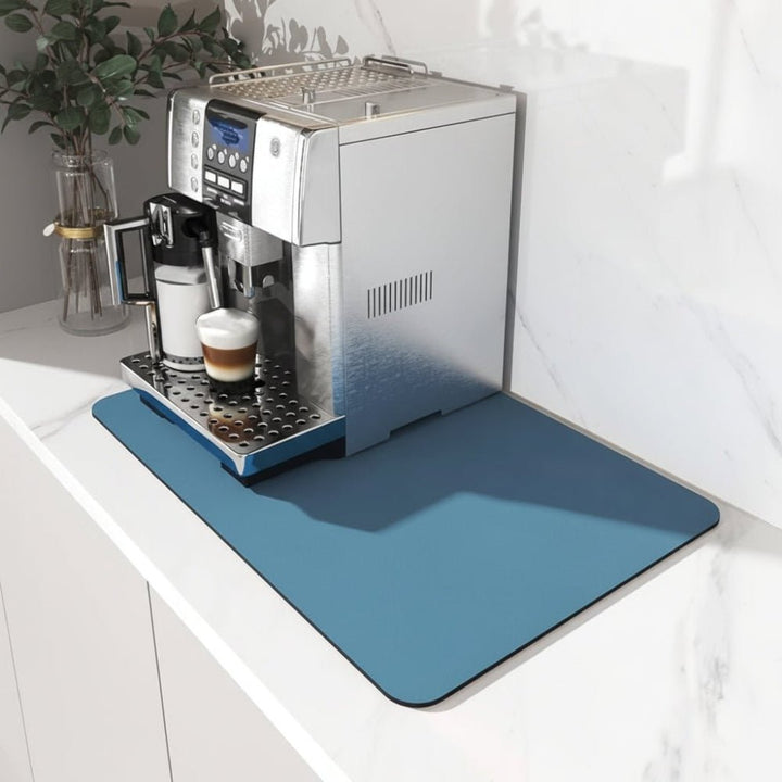 Solid blue rectangular mat with rounded corners under a silver espresso machine on a white marble counter 1