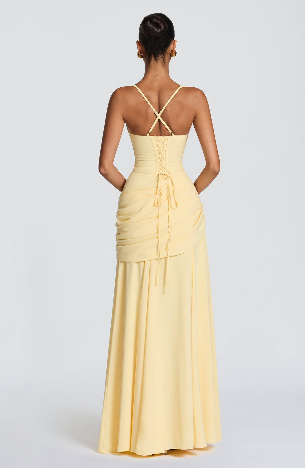 Back view of the pale yellow gown showing the lace-up corset back, crossed thin straps and draped hip detail.