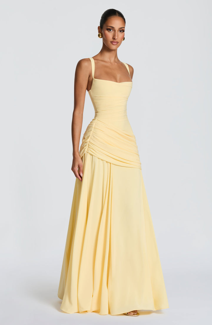 Three-quarter side view of the pale yellow maxi dress, showing the ruched waist, draped hip and full flowing skirt.